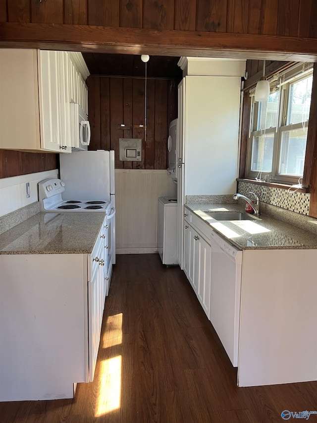 kitchen with a sink, dark wood-style floors, stacked washing maching and dryer, white appliances, and white cabinets