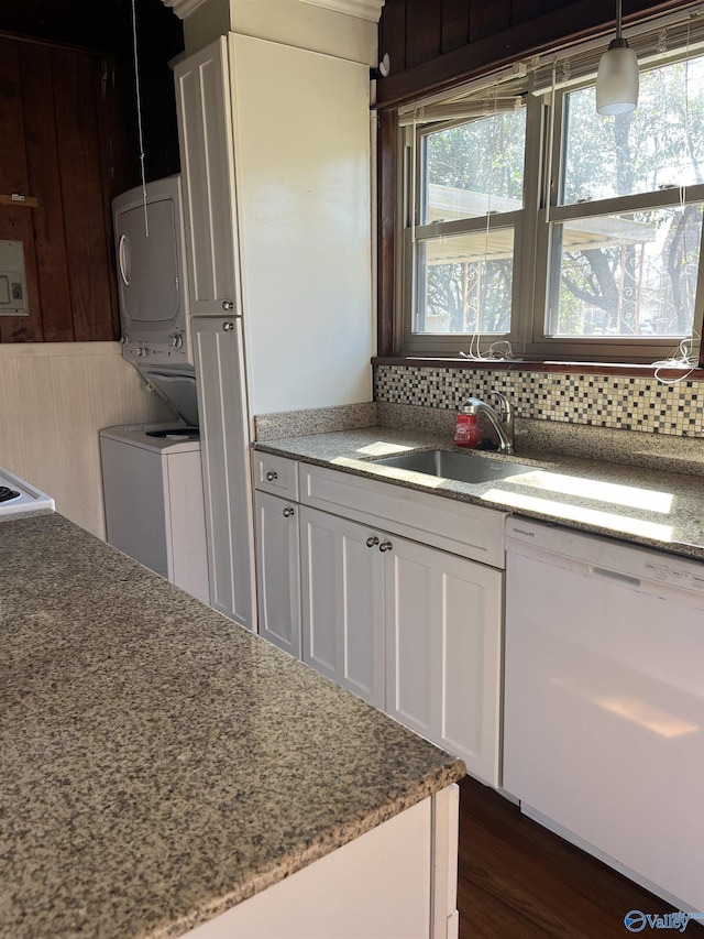 kitchen with dishwasher, stacked washing maching and dryer, dark wood-style floors, white cabinets, and a sink