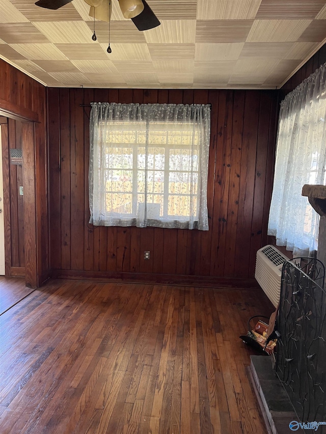 empty room with hardwood / wood-style floors, a ceiling fan, and wood walls