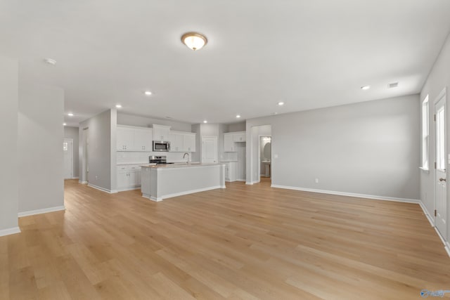 unfurnished living room featuring baseboards, light wood-type flooring, recessed lighting, and a sink