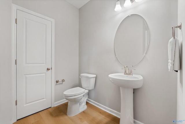 half bath with baseboards, wood finished floors, toilet, and a sink