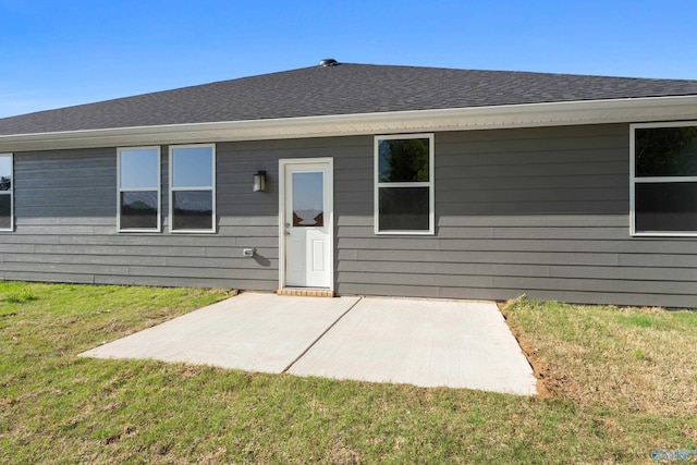 rear view of house featuring a lawn, roof with shingles, and a patio area