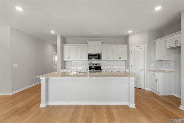 kitchen with decorative backsplash, appliances with stainless steel finishes, a sink, white cabinetry, and a center island with sink