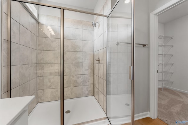 bathroom featuring a walk in closet, a shower stall, and baseboards