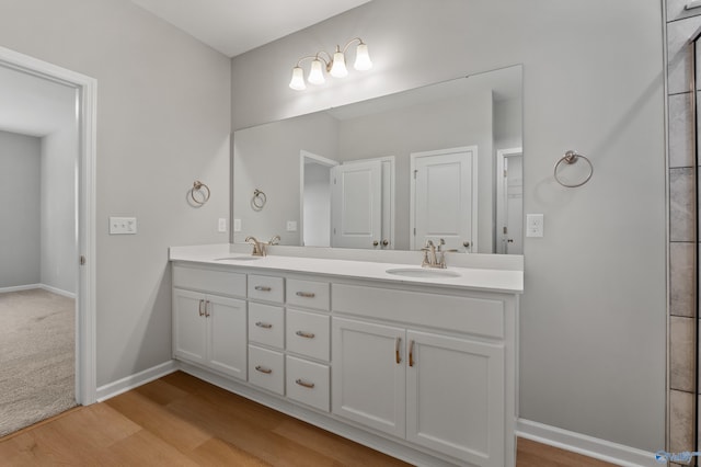 bathroom with double vanity, a sink, wood finished floors, and baseboards