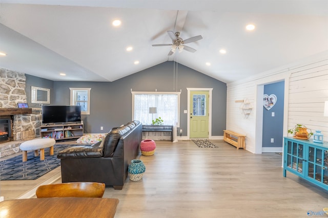 living room featuring ceiling fan, a stone fireplace, lofted ceiling, and light hardwood / wood-style floors