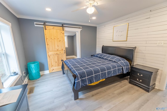 bedroom with ceiling fan, wooden walls, ornamental molding, a barn door, and light wood-type flooring