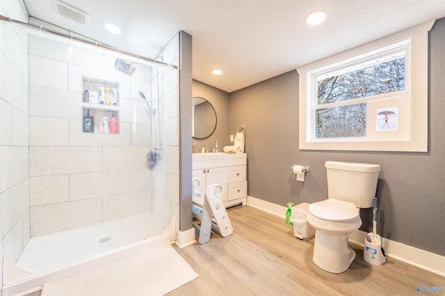 bathroom featuring vanity, a tile shower, hardwood / wood-style floors, and toilet