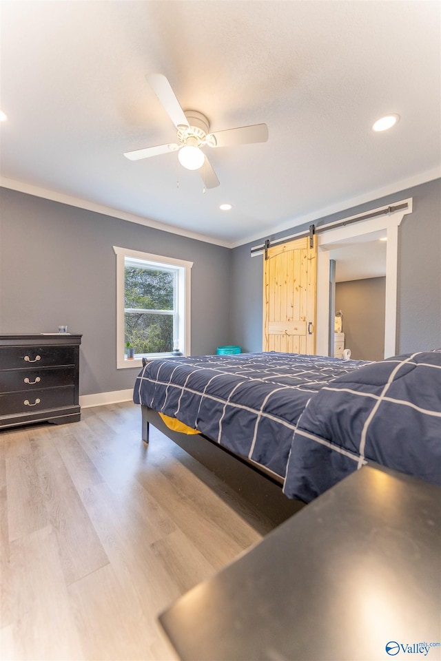bedroom featuring ceiling fan, ornamental molding, wood-type flooring, and a barn door