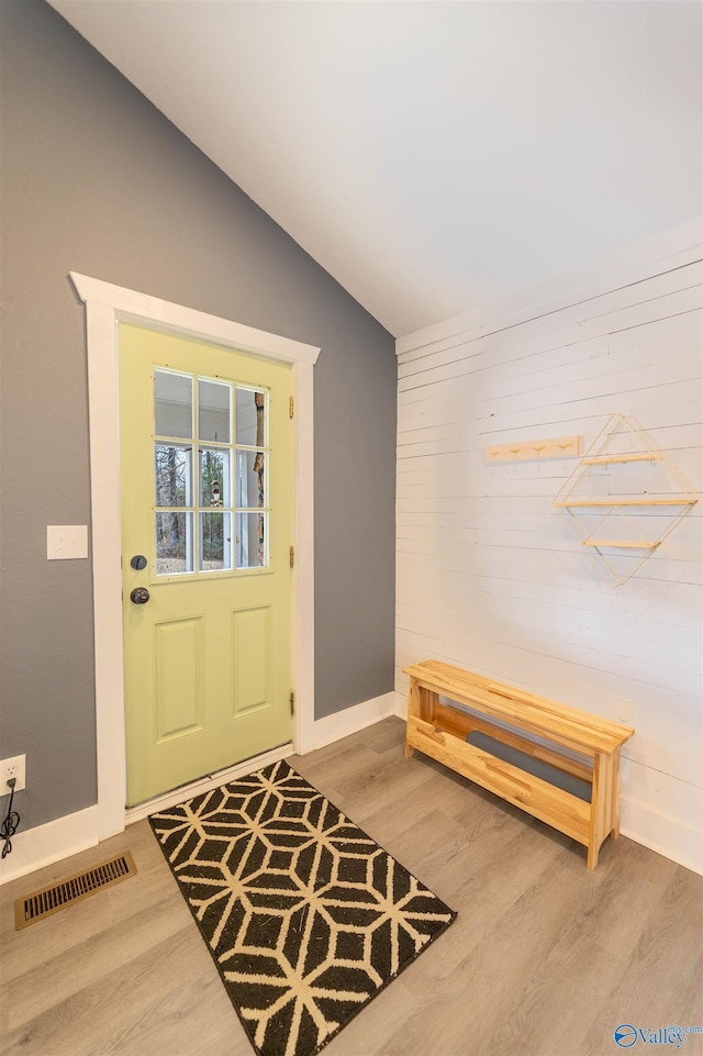 foyer with vaulted ceiling, wood-type flooring, and wooden walls