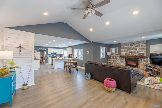 living room with lofted ceiling, a stone fireplace, light hardwood / wood-style flooring, and ceiling fan