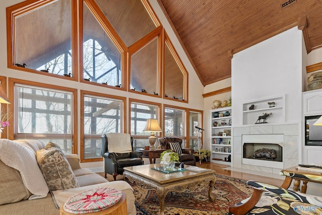 living room featuring high vaulted ceiling, a tiled fireplace, hardwood / wood-style flooring, wooden ceiling, and built in shelves