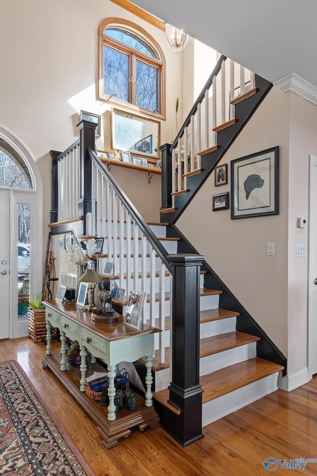 staircase with hardwood / wood-style flooring, ornamental molding, a chandelier, and a towering ceiling