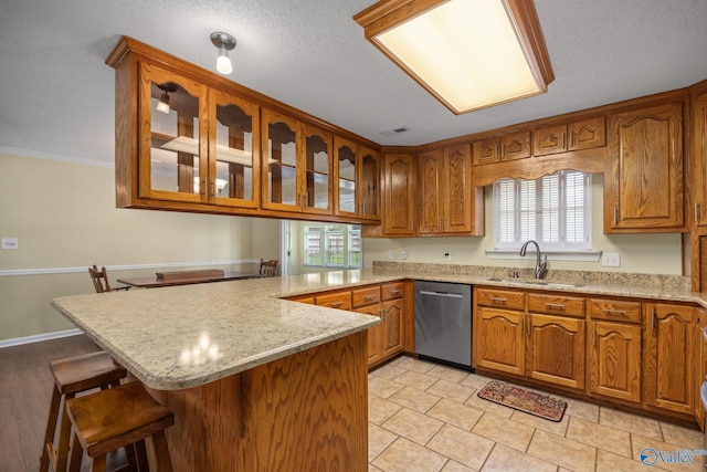 kitchen featuring sink, dishwasher, light stone counters, a kitchen bar, and kitchen peninsula