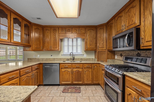 kitchen featuring light stone counters, appliances with stainless steel finishes, sink, and light tile patterned floors