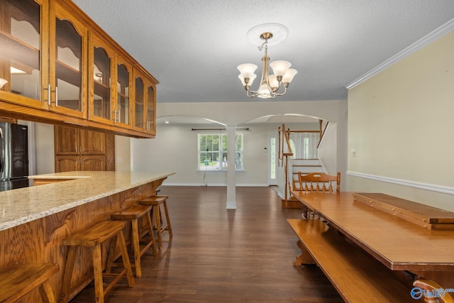 kitchen with black refrigerator, hanging light fixtures, a notable chandelier, light stone counters, and dark wood-type flooring