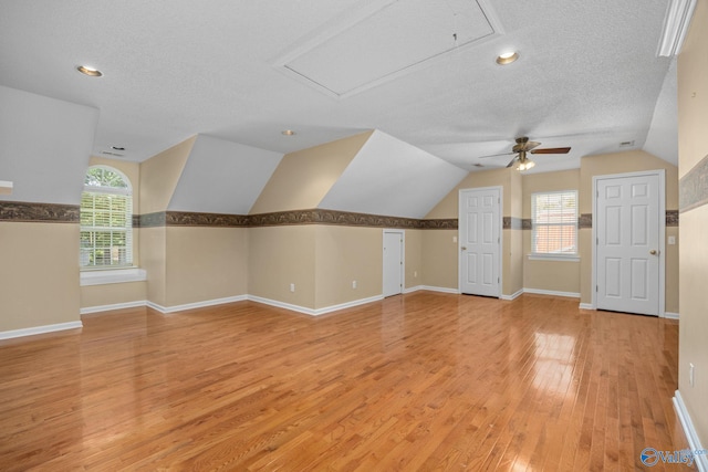 additional living space featuring a textured ceiling, plenty of natural light, vaulted ceiling, and light wood-type flooring