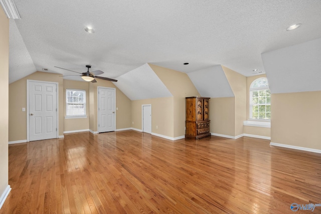 additional living space featuring lofted ceiling, ceiling fan, light hardwood / wood-style flooring, and a textured ceiling