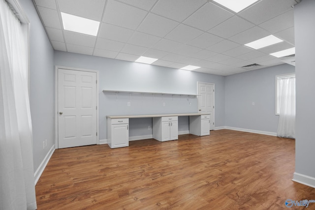 unfurnished office featuring a paneled ceiling, built in desk, and light hardwood / wood-style floors