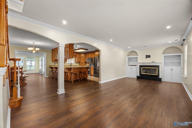 living room featuring built in shelves, dark wood-type flooring, ornamental molding, and a textured ceiling