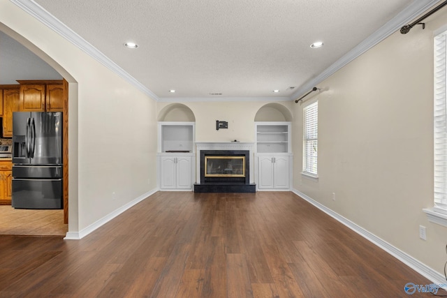 unfurnished living room featuring built in features, ornamental molding, a premium fireplace, dark wood-type flooring, and a textured ceiling