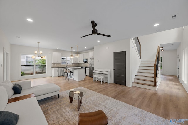 living area with light wood-type flooring, a ceiling fan, stairway, and recessed lighting