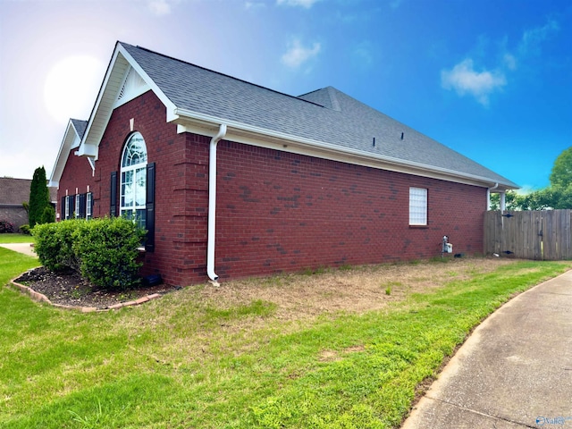 view of side of home featuring a lawn, roof with shingles, fence, and brick siding