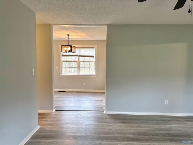 unfurnished room with a textured ceiling, ceiling fan with notable chandelier, and hardwood / wood-style flooring