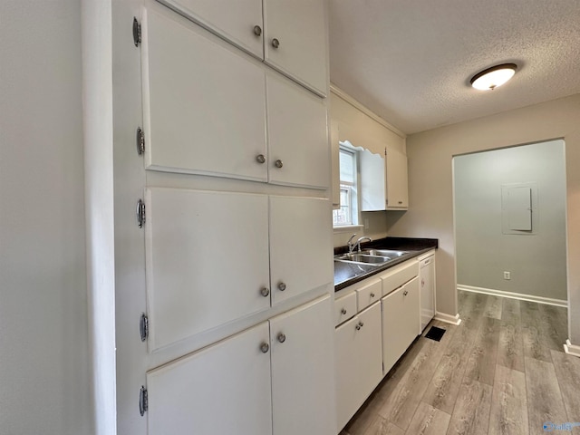 kitchen with white cabinets, a textured ceiling, light hardwood / wood-style flooring, and sink