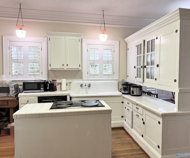 102 Jackson St, Albertville, AL 35950 - kitchen with stainless steel microwave, tile counters, black electric cooktop, ornamental molding, and dark wood-type flooring