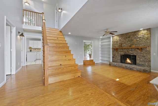 unfurnished living room with a ceiling fan, wood finished floors, stairway, a stone fireplace, and baseboards