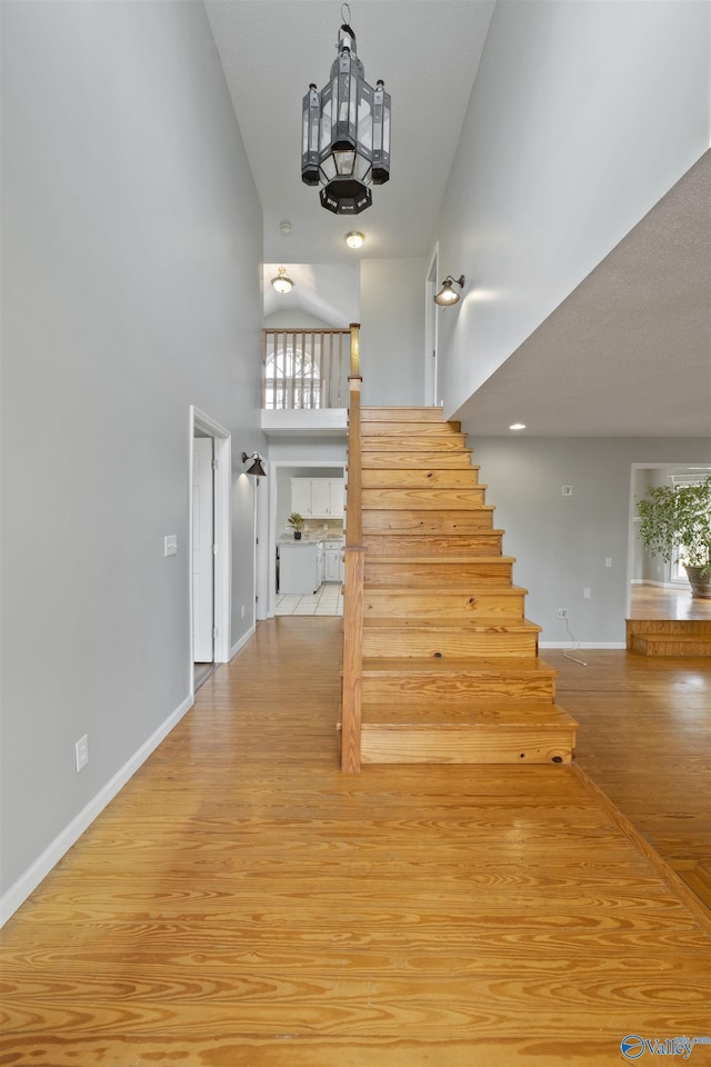 stairway with a high ceiling, wood finished floors, and baseboards