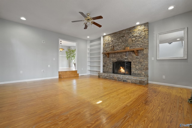 unfurnished living room with built in features, wood finished floors, a fireplace, baseboards, and ceiling fan