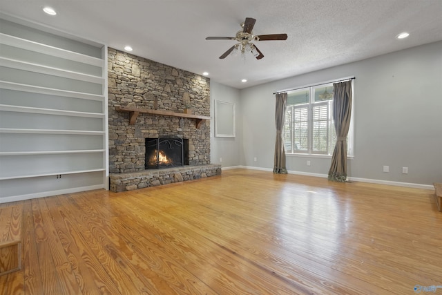 unfurnished living room featuring a ceiling fan, a textured ceiling, wood finished floors, a fireplace, and baseboards