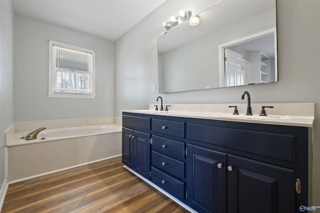 bathroom featuring double vanity, a garden tub, wood finished floors, and a sink