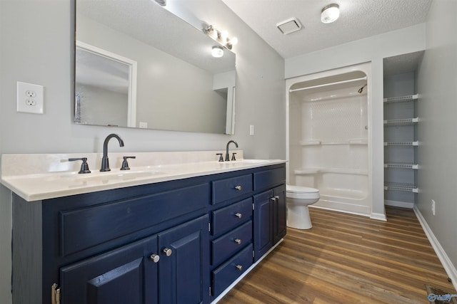 bathroom with toilet, double vanity, wood finished floors, a textured ceiling, and a sink