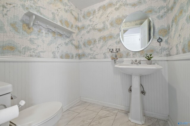 bathroom featuring wallpapered walls, a wainscoted wall, and marble finish floor