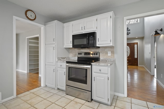 kitchen with light tile patterned floors, stainless steel range with electric stovetop, white cabinets, black microwave, and backsplash