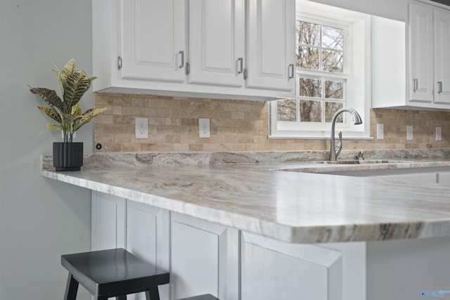 kitchen with decorative backsplash, white cabinets, light stone countertops, and a sink