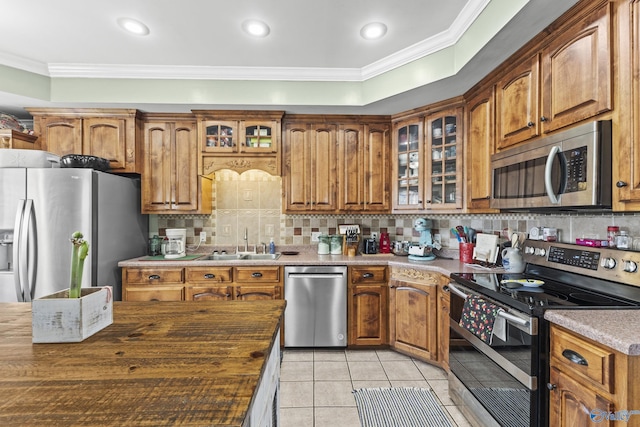 kitchen with light tile patterned flooring, sink, crown molding, appliances with stainless steel finishes, and backsplash