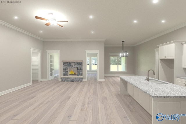 kitchen featuring light stone countertops, light wood-type flooring, sink, white cabinets, and a stone fireplace