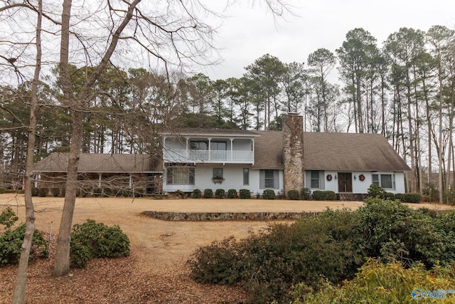view of front of home featuring a chimney, a balcony, and a shingled roof