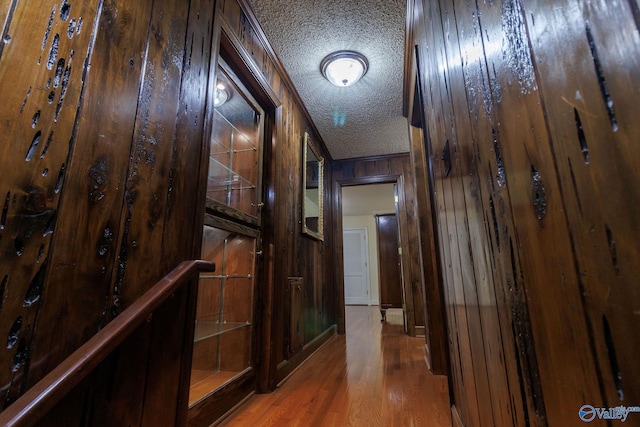 hall with wood-type flooring, wooden walls, and a textured ceiling