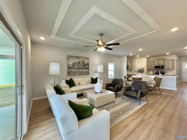 living room featuring light wood-style flooring, a raised ceiling, recessed lighting, and a ceiling fan