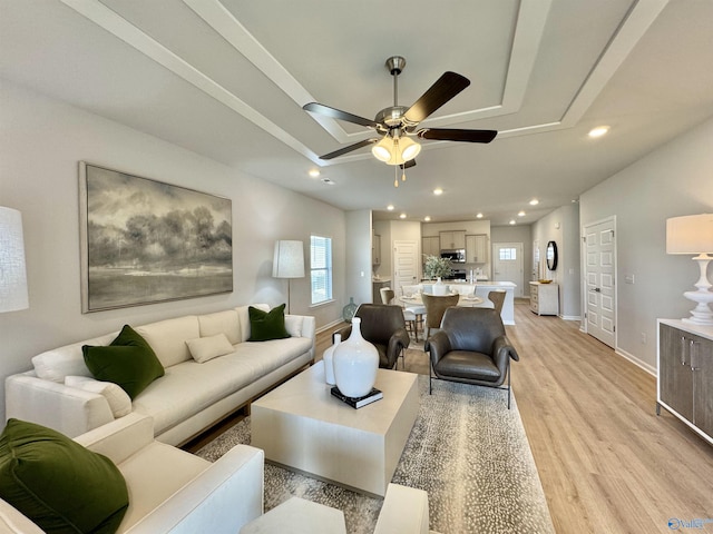 living area featuring baseboards, light wood-type flooring, ceiling fan, and a raised ceiling