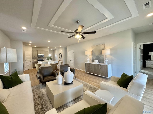 living room with a tray ceiling, visible vents, a ceiling fan, and light wood-type flooring