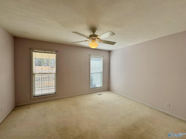 carpeted spare room with ceiling fan, a healthy amount of sunlight, and a textured ceiling