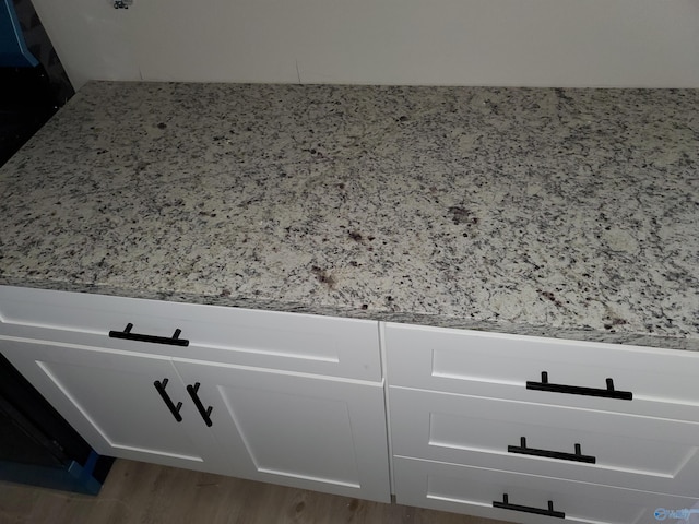 interior details featuring light stone counters, wood-type flooring, and white cabinets