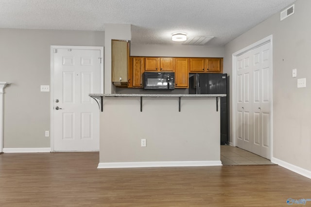 kitchen with black appliances, visible vents, brown cabinetry, and a kitchen breakfast bar