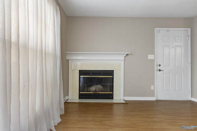 unfurnished living room with wood finished floors, a glass covered fireplace, and baseboards